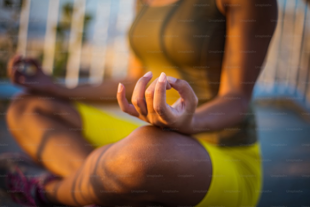 African young woman in nature sitting in yoga position on the bridge. Focus is on hand.