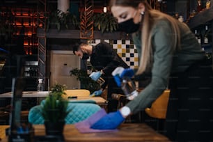 Giovani camerieri di ristoranti che puliscono e disinfettano tavoli e superfici contro la pandemia di Coronavirus. Indossano maschere protettive e guanti.