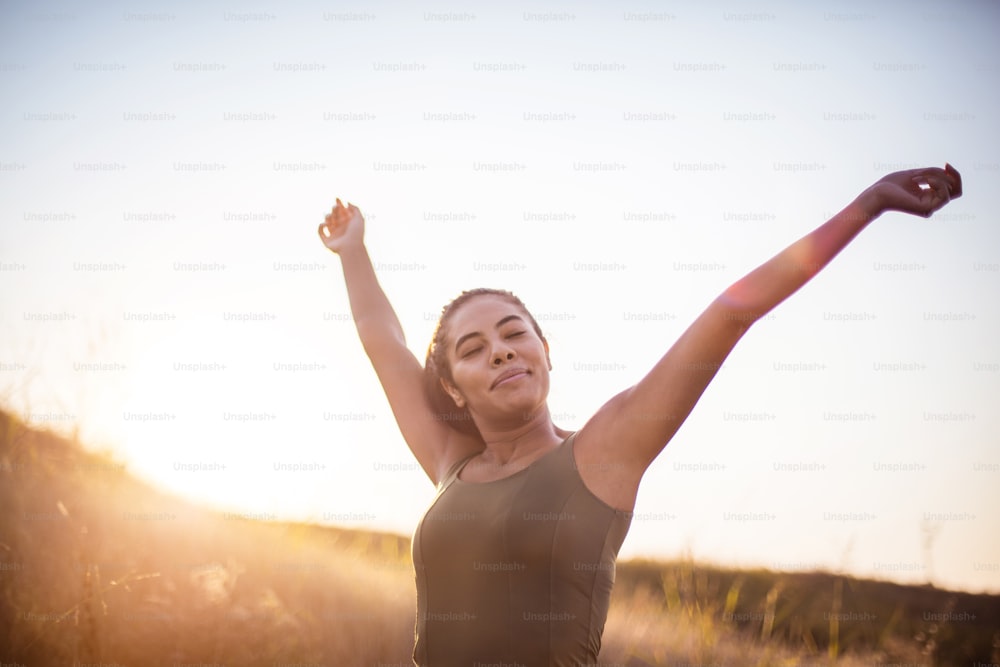 African woman standing in the nature with closed eyes and outstretched arms.