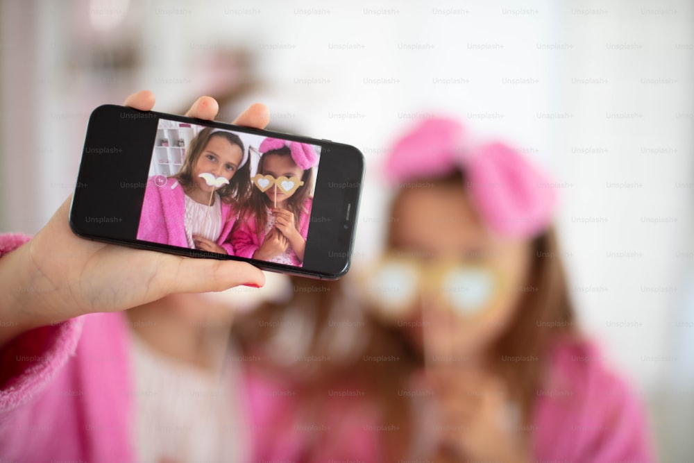 Deux petites filles jouant dans la pièce et prenant un autoportrait. L’accent est mis sur le mobile.