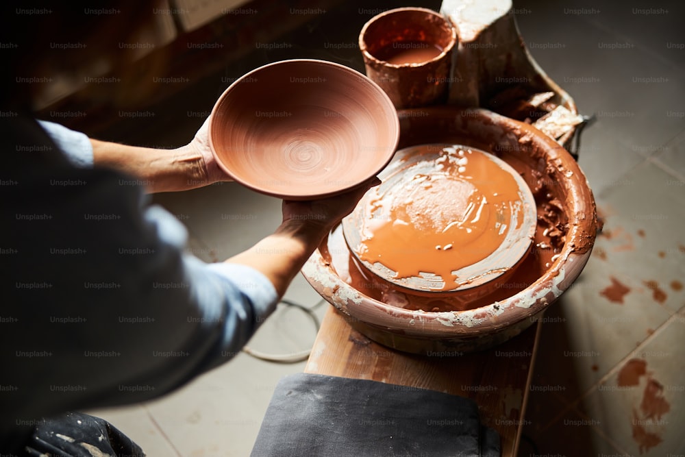 スタジオでろくろのそばに立って陶器のボウルを持っている女性の陶芸家の接写