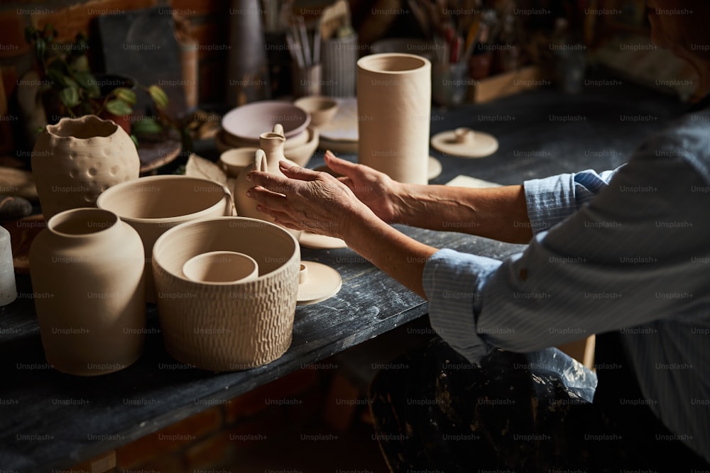 Close up of senior woman potter sitting at the table with earthenware in pottery studio