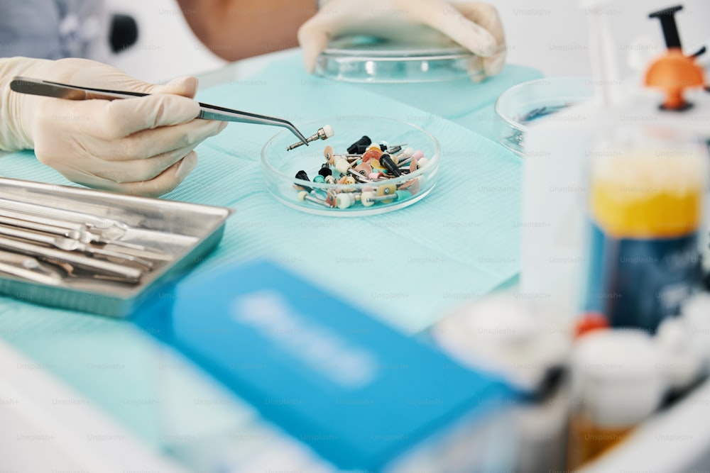 Baumwollzange hebt eine Zahnpolierbürste von Glastablett mit vielen Gegenständen auf dem medizinischen Tisch