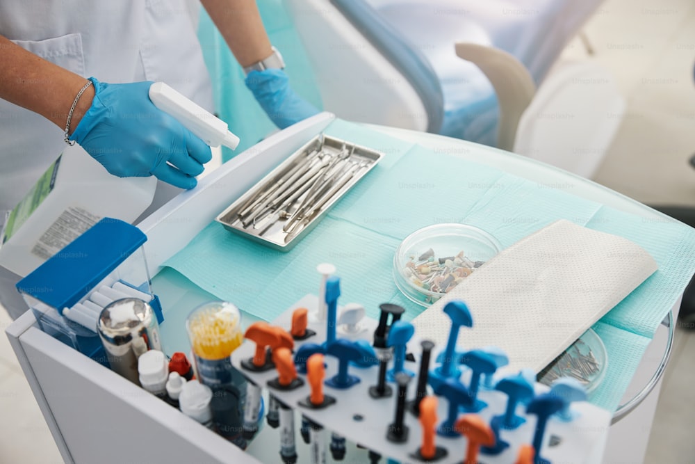 Dental practitioner leaning cleaning detergent container over steel tray of stomatological tools during their disinfection process