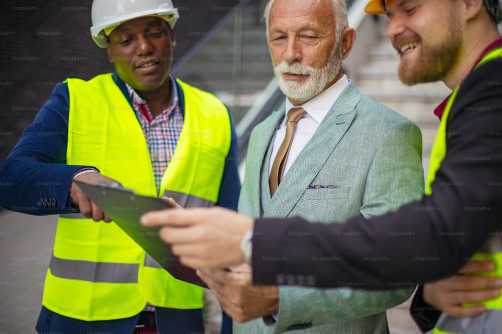 The construction site boss has a conversation with the architects. Reading document. Focus is on background.