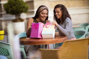 Two women in café sitting and looking in shopping bag.