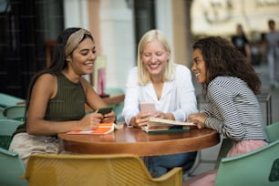 Three students reading books in café and talking. Focus is on background.