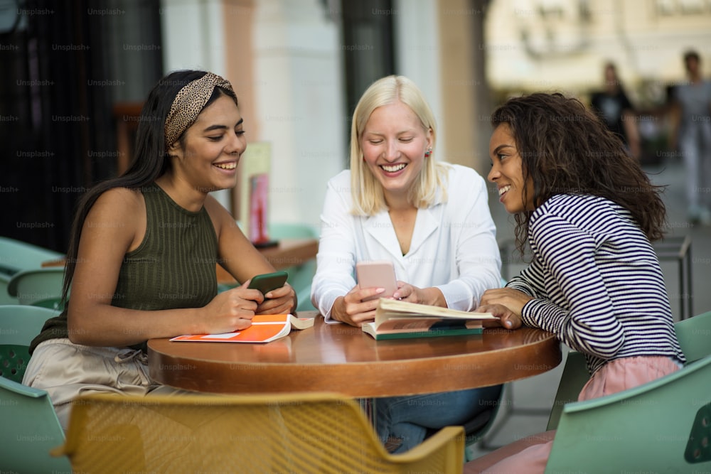 Three students reading books in café and talking. Focus is on background.