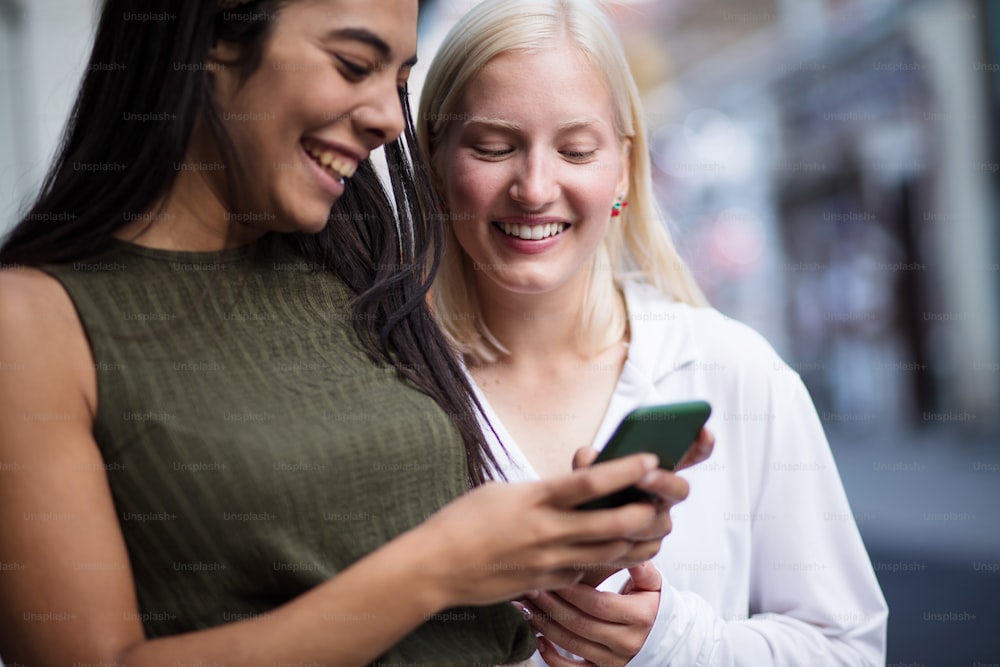 Two women on street using phone together. Focus is on blond woman.