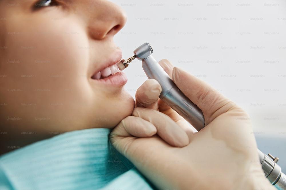 Side view of child face and hand, keeping dental handpiece with polishing bristle, while using it on patient teeth