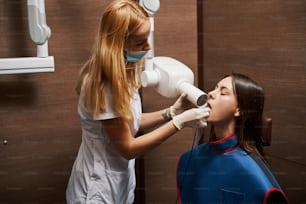 Careful dental practitioner putting x-ray film in plastic bag inside female mouth while examining it with dental radiography apparatus
