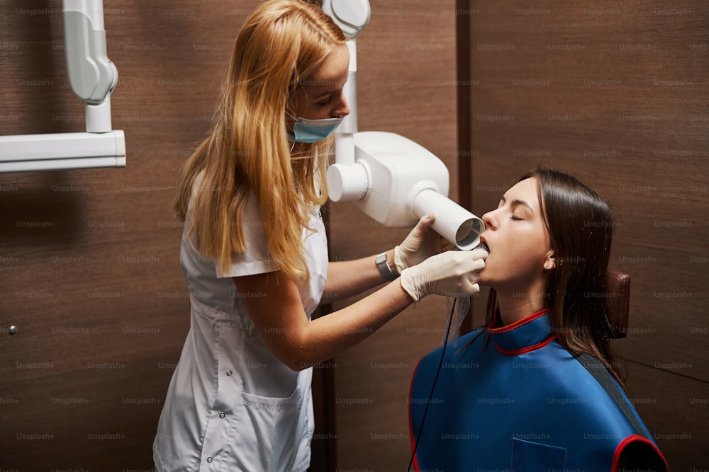 Dentista attento che mette la pellicola a raggi X in un sacchetto di plastica all'interno della bocca femminile mentre la esamina con l'apparecchio di radiografia dentale