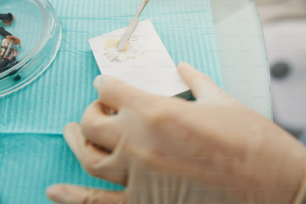 Orthodontist blending together dental cement powder with oil during tooth filling creation on brick from foam plastic