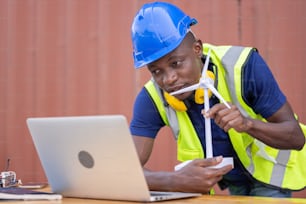 Engineer African American black worker discussing of solar energy from wind turbine model and online with laptop at construction site.
