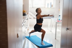 Affascinante signora afroamericana in abbigliamento sportivo che fa esercizio di yoga e sorride mentre si allena al mattino nel suo appartamento