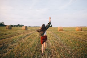 Beautiful carefree woman throw up hat in the sky and smiling in evening summer field. Happiness. Young happy female relaxing and having fun in countryside. Atmospheric moment