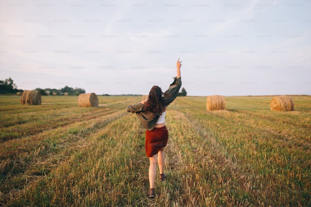 Beautiful carefree woman throw up hat in the sky and smiling in evening summer field. Happiness. Young happy female relaxing and having fun in countryside. Atmospheric moment