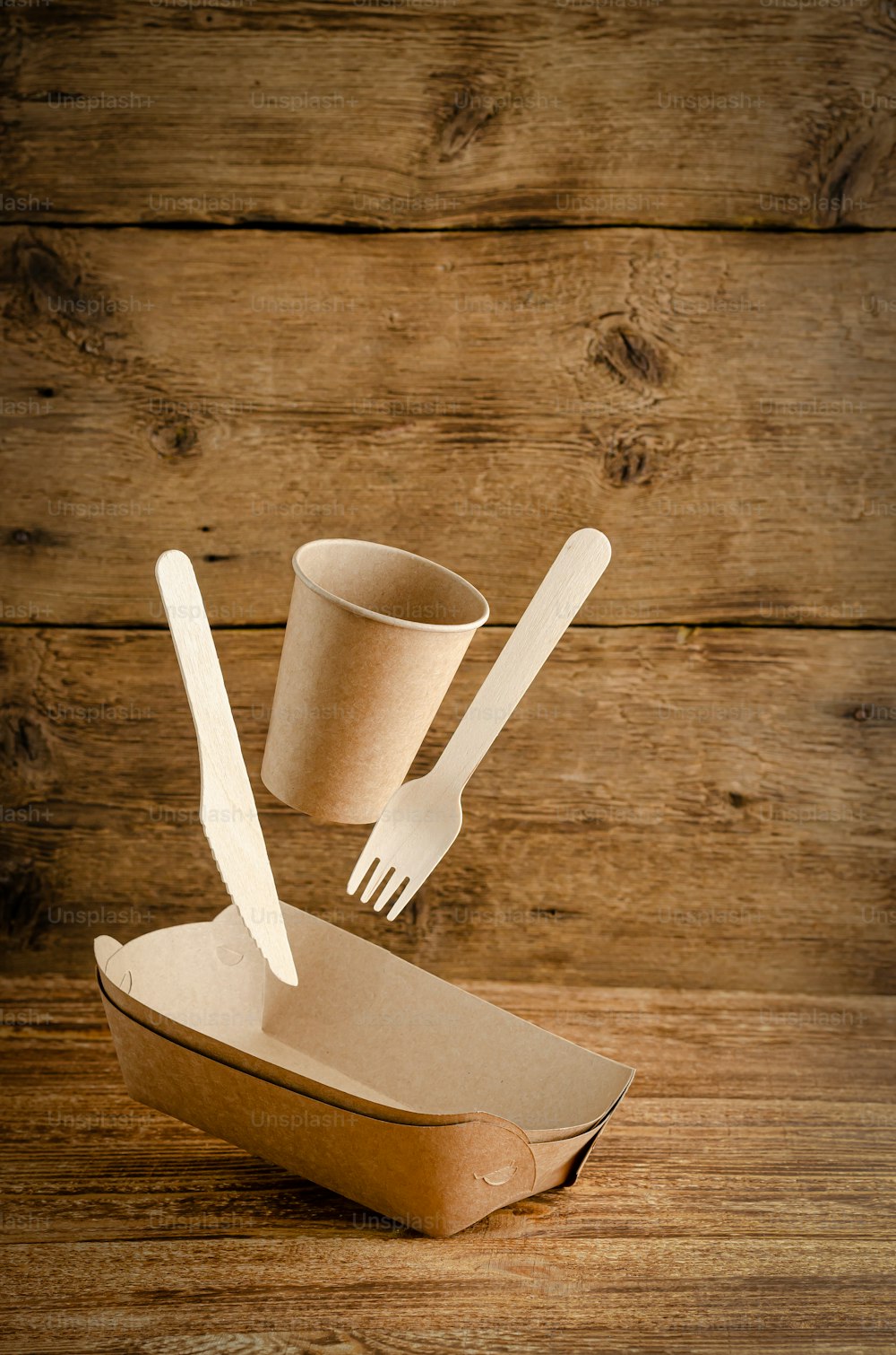 Flying disposable paper tableware on wooden background. Environmental care concept. Copy space.
