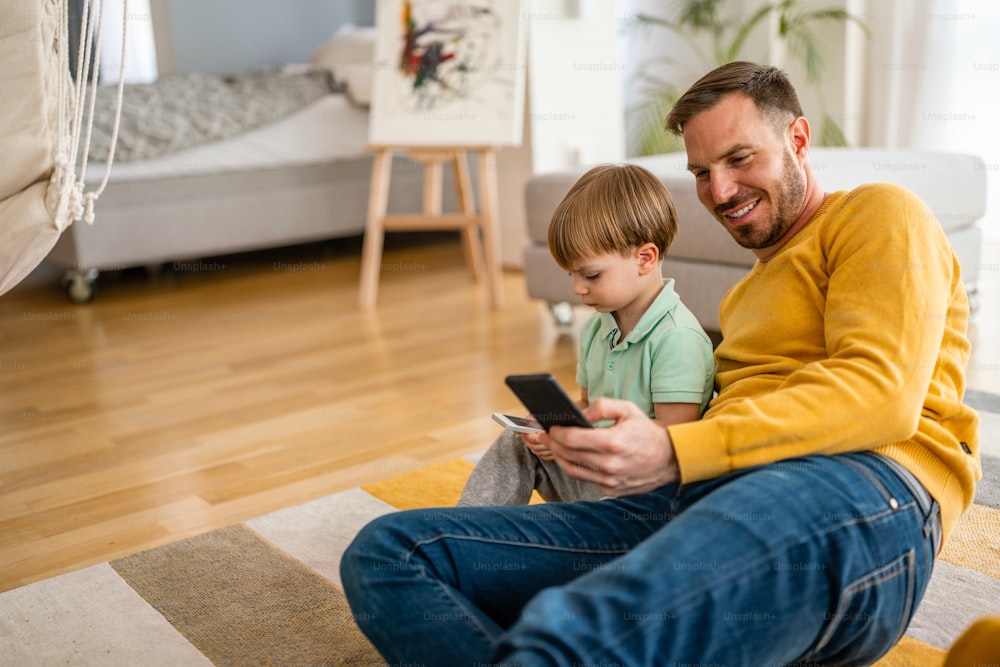 Glücklicher Vater und Sohn spielen zu Hause auf dem Handy. Technologiesucht Familienproblemkonzept