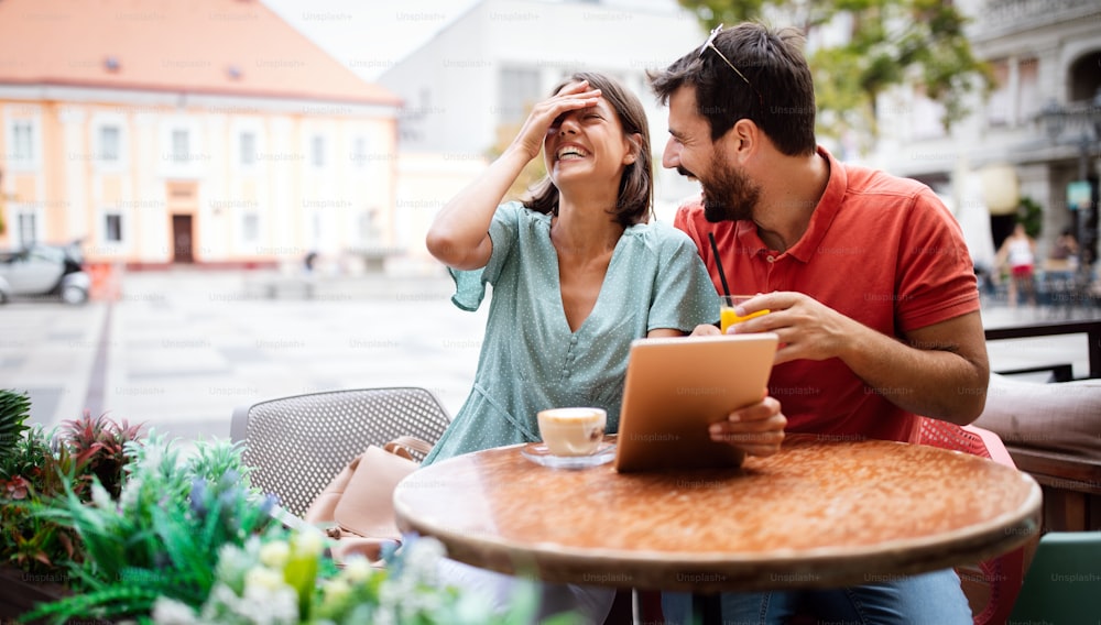Happy embracing couple using tablet, smiling and talking in cafe