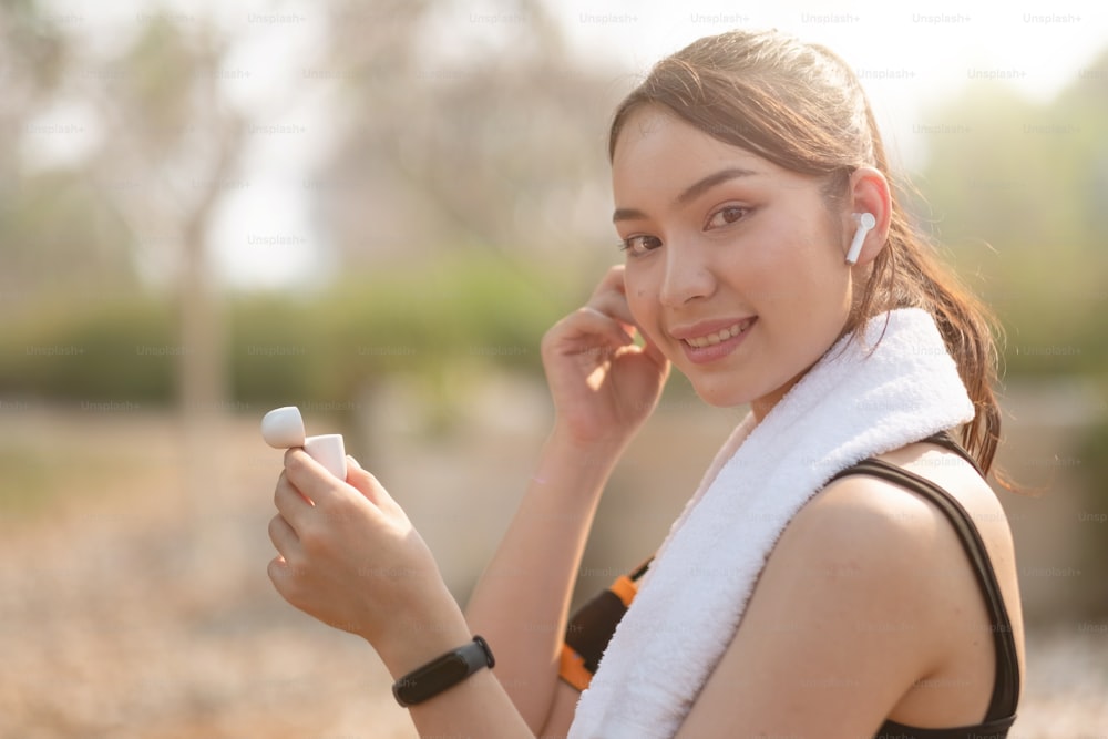 Foto de una hermosa joven asiática que corre al aire libre escuchando música con auriculares.