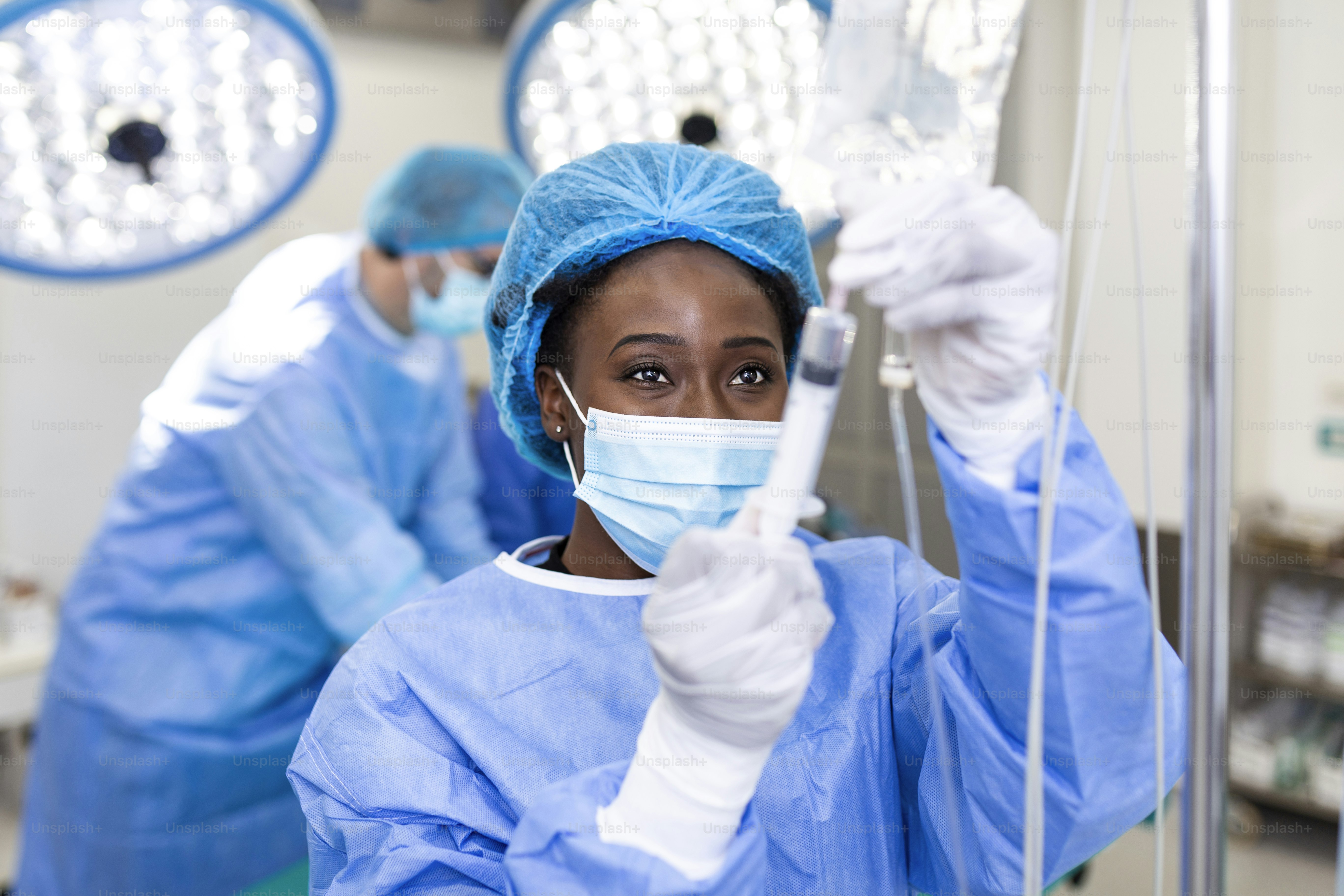 African american female Doctor in the operating room putting drugs through an IV - surgery concepts