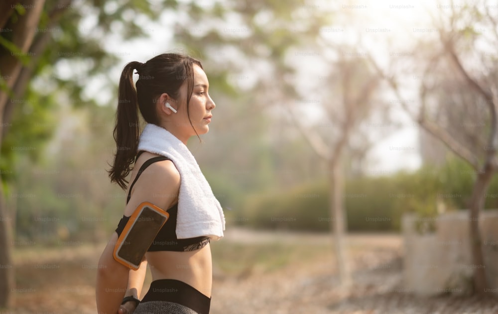 Aufnahme einer jungen, hübschen asiatischen Athletin, die sich nach dem Joggen mit Ohrhörern gegen den Park ausruht