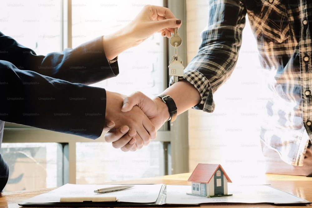 不動産業者と顧客は、住宅保険と投資ローン、握手と取引の成功について、契約の完了を祝う握手を交わしています