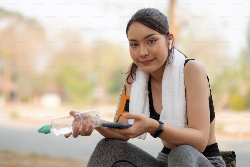 Portrait fitness woman sweating taking a break listening to music on phone after difficult training.