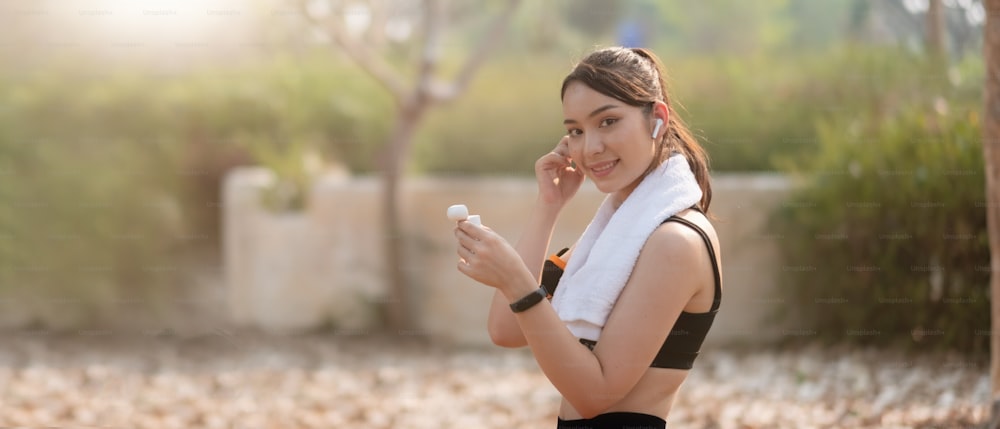 Foto de una hermosa joven asiática que corre al aire libre escuchando música con auriculares.