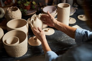 手作りの陶器で木製の机に座って白い粘土鍋の白に触れる年配の女性陶芸家の接写