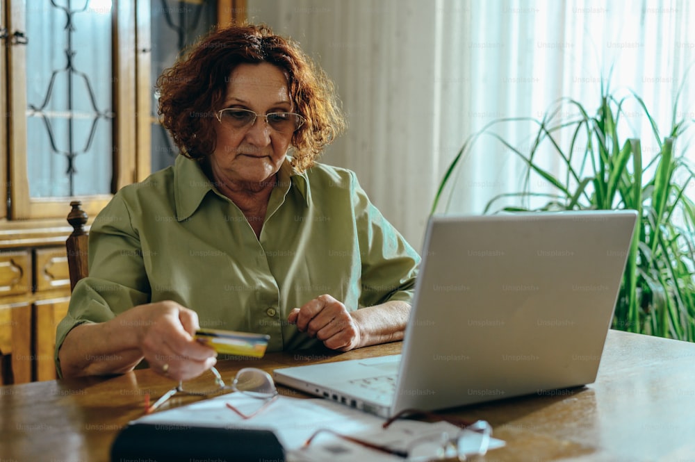 Femme âgée utilisant un ordinateur portable et une carte de crédit lors de ses achats en ligne à la maison