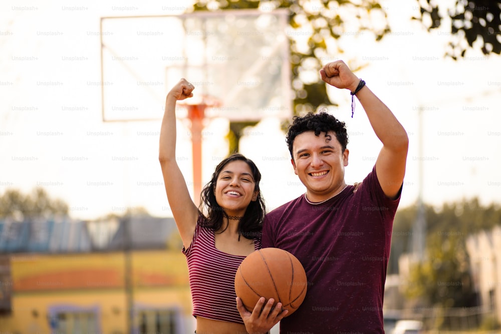 Couple with arms raised standing on basketball court and holding ball.