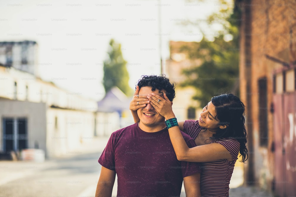 Young couple on the street. Girl holding hands on eyes to her boyfriend.