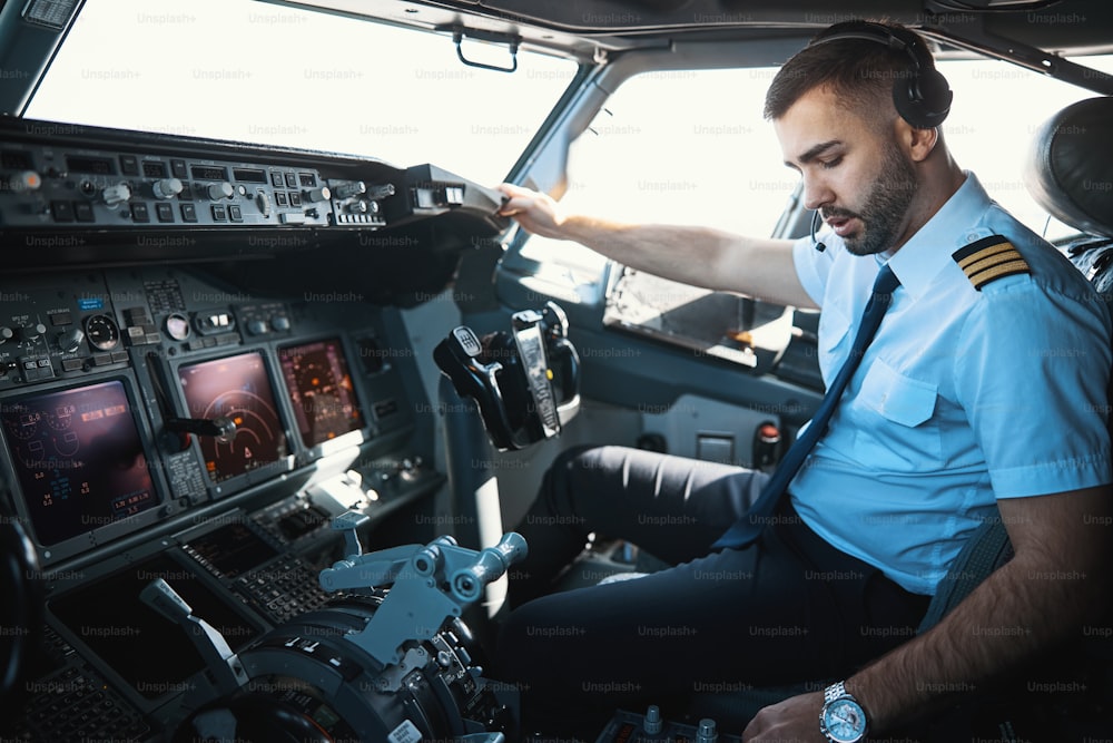 Ernsthafter Mann sitzt in einem Cockpit und schaut auf die Griffe unten des Bedienfelds
