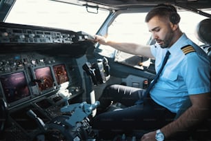 Homme sérieux assis dans un cockpit et regardant les poignées baissées du panneau de commande