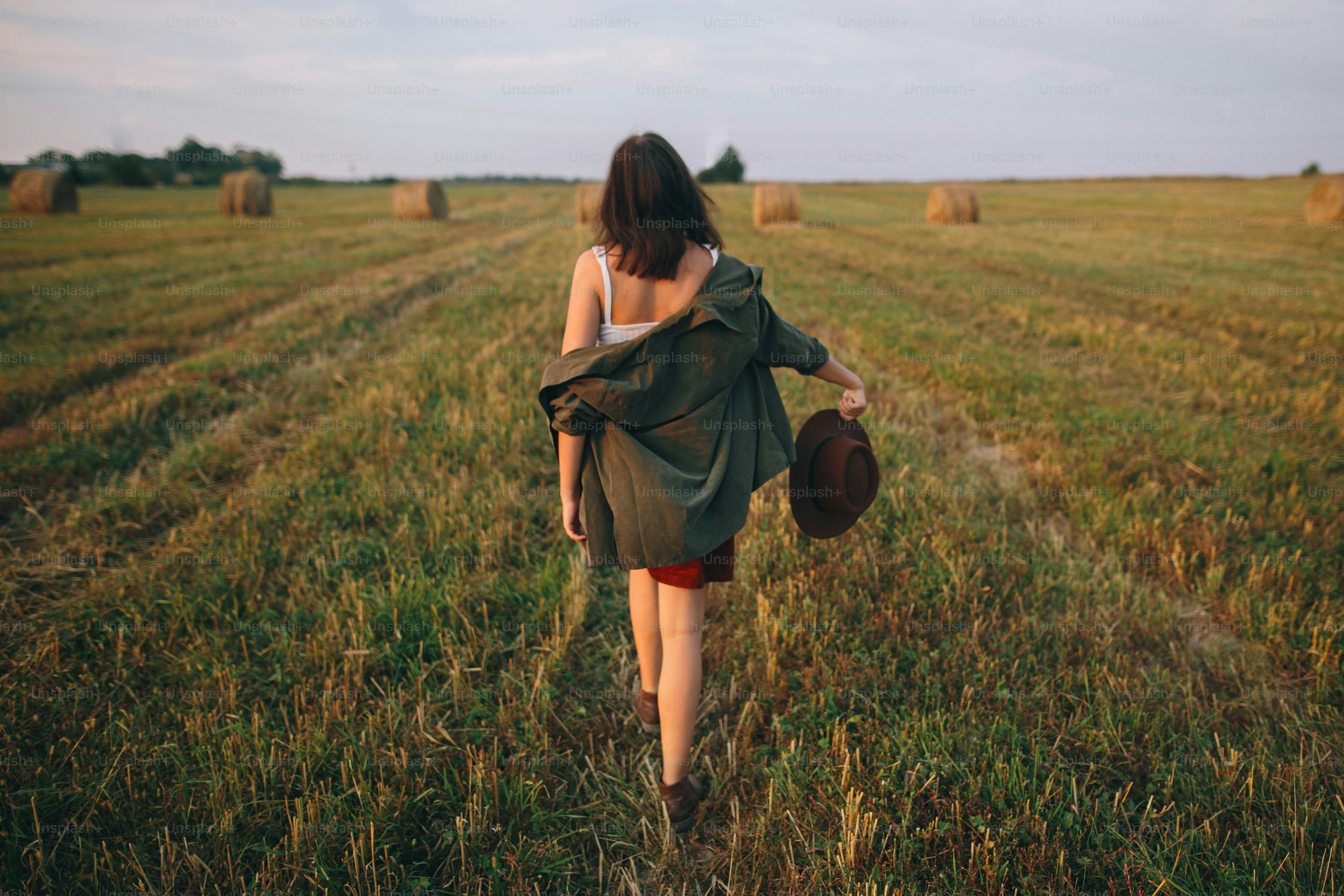 저녁 여름 들판을 걷고 있는 모자를 쓴 아름다운 평온한 여자. 젊은 행복하고 세련된 여성은 시골에서 휴식을 취하고 춤을 추며 저녁을  즐긴다. 대기 순간. 뒷면보기 사진 – Unsplash의 해질녘 이미지, image size:3000x2000