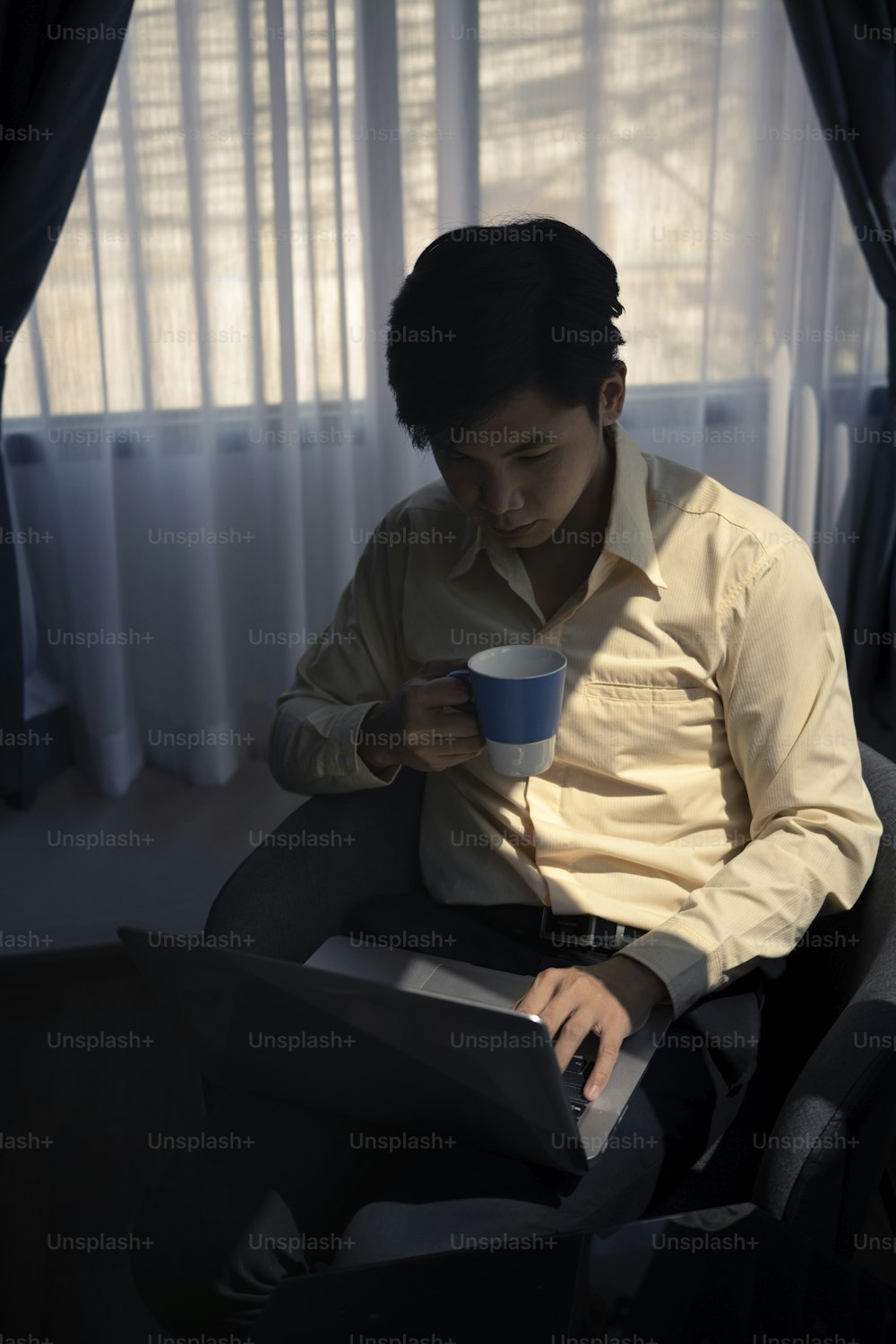 コーヒーカップを持ち、オフィスで朝にコンピューターのラップトップでニュースを読んでいる若い実業家の肖像画。