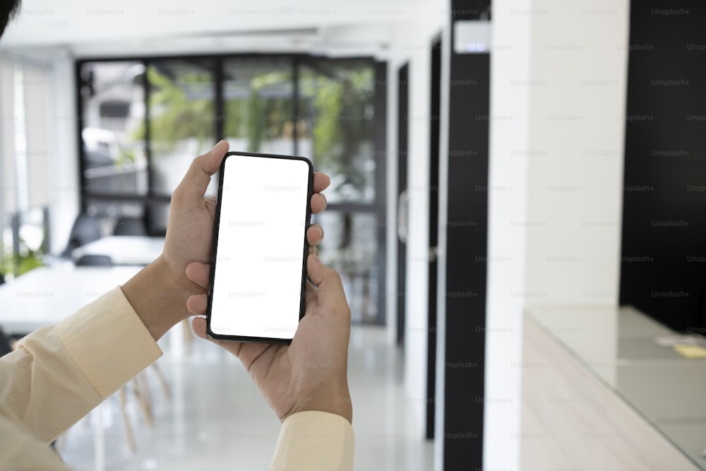 Mock-up-Bild des Geschäftsmannes Hans, der ein Mobiltelefon mit leerem Bildschirm in der Büroeinrichtung hält.