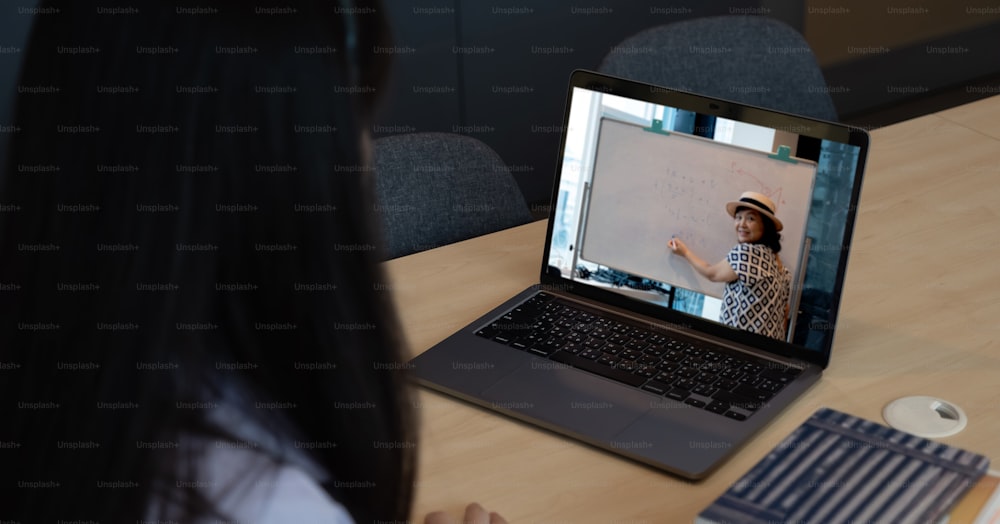 Studentessa asiatica che impara la classe online online su Internet virtuale dall'insegnante di scuola tramite riunione a distanza a causa della pandemia di covid. Insegnamento femminile con l'uso di cuffie e lavagna.