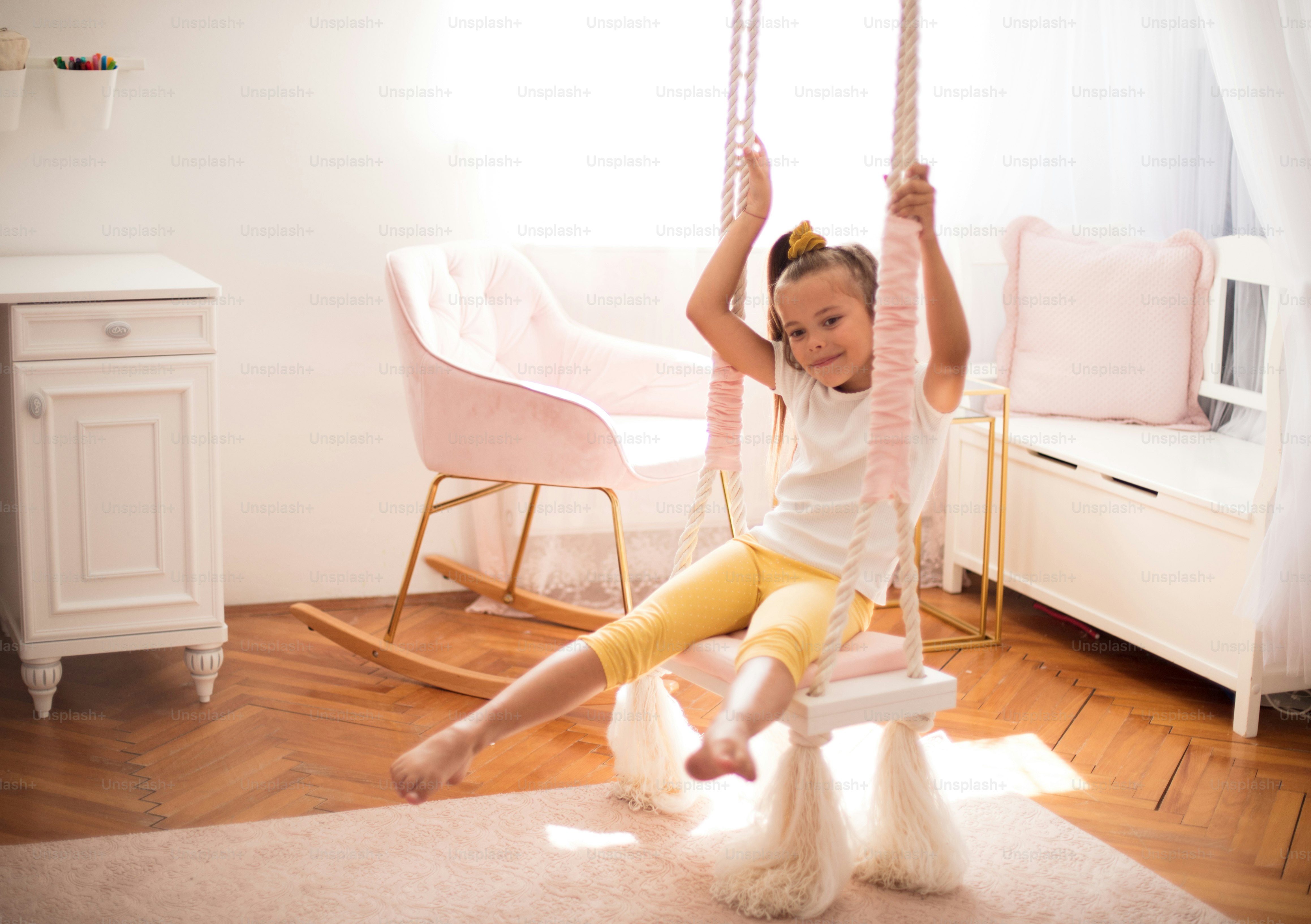 Portrait of smiling little girl on swing in her bedroom.