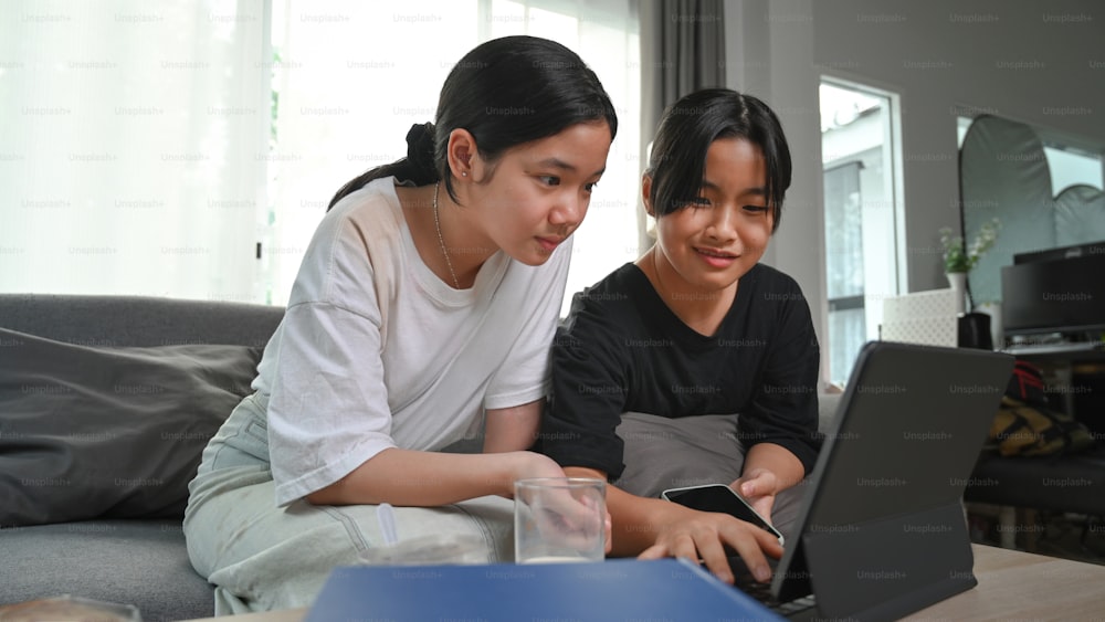 Deux jeunes filles asiatiques utilisant une tablette d’ordinateur tout en étant assis ensemble sur le canapé dans le salon.