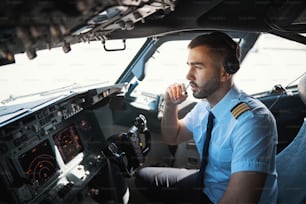 Junger kaukasischer Pilot runzelt die Stirn, während er tagsüber im Cockpit sitzt und über den Sender kommuniziert