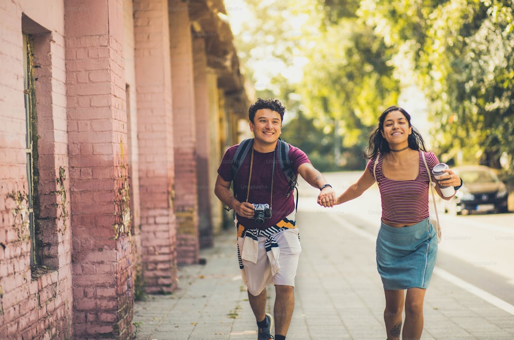 Young couple running trough street and holding hands.  Man with camera and girl with cup of coffee.