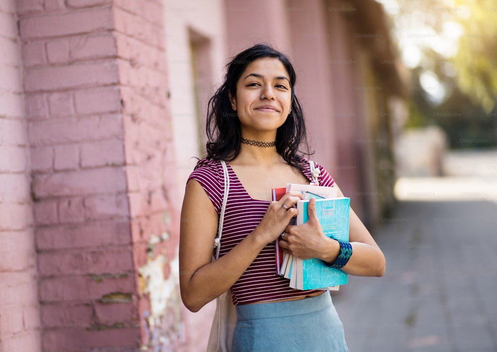 Young student woman standing on street and holding books.