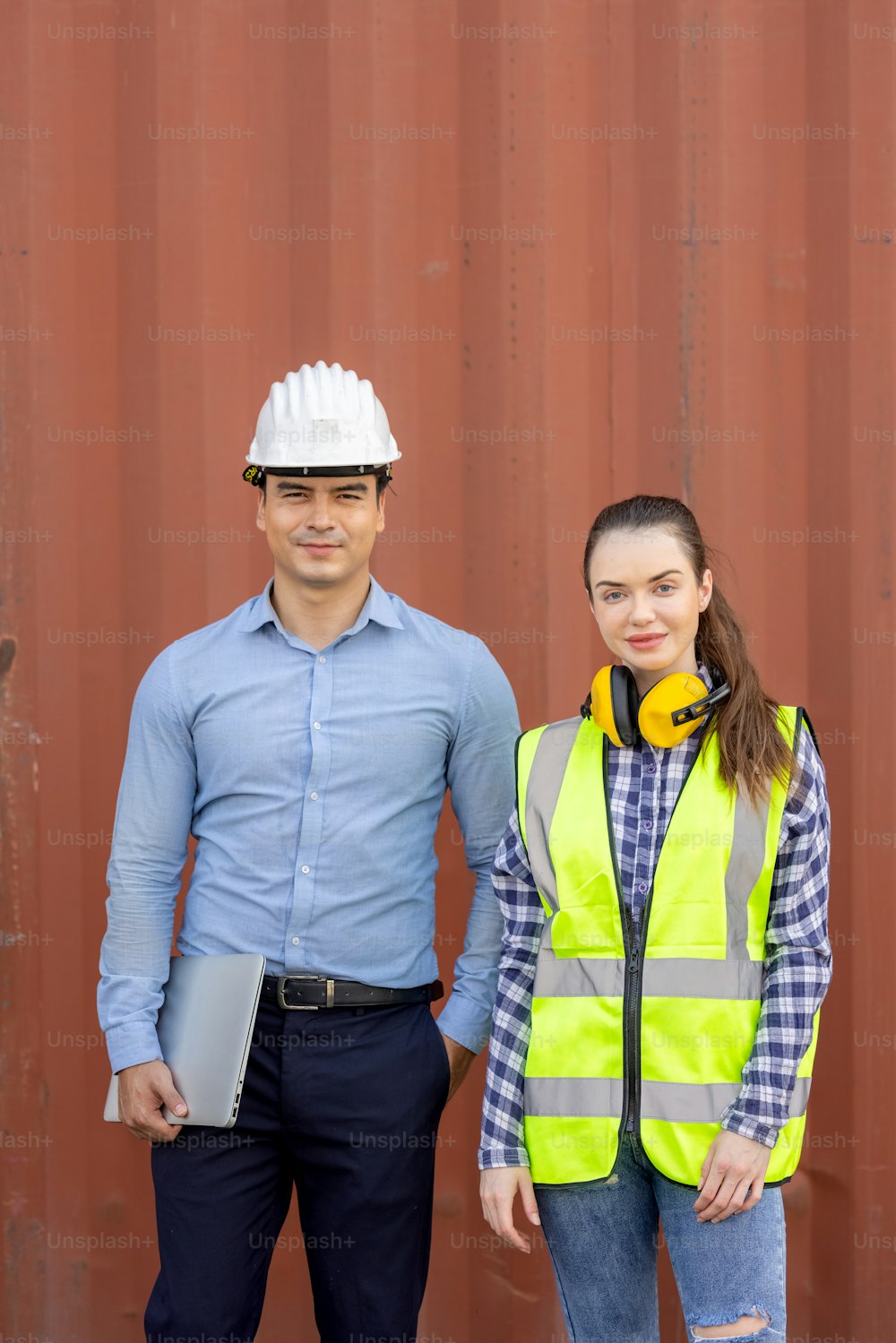 Confident engineers portrait in uniforms standing in front of the containers. Logistics and shipping. Professional occupation.