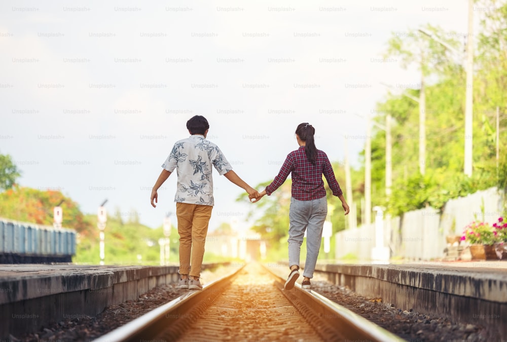 Young couple walking hand in hand on railway tracks, along railroad together