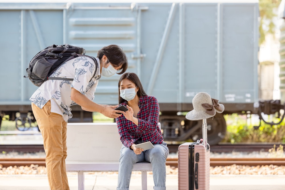 Mochila de viajero masculino joven con máscara y móvil en la mano pidiendo ayuda a una mujer sentada y señalando en las escaleras del metro, distancia covid