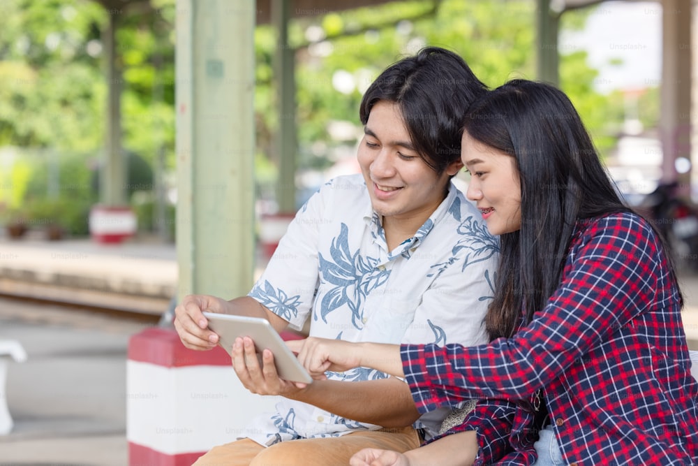 Mochileiro jovem casal asiático usando tablet para encontrar viagem de destino na estação ferroviária