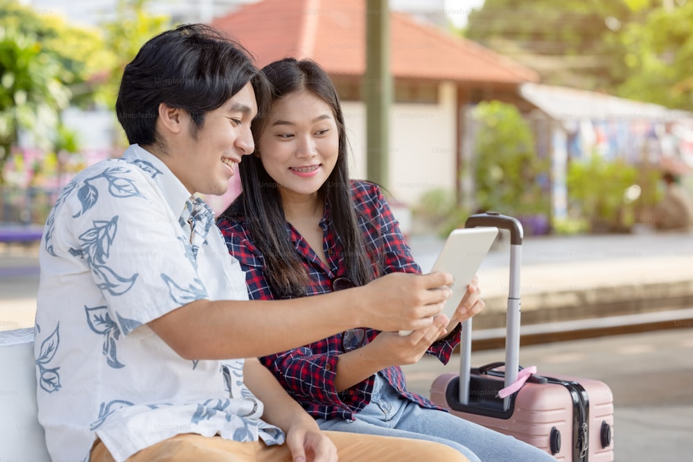 Joven mochilero de pareja asiática usando tableta para encontrar viaje de destino en la estación de tren